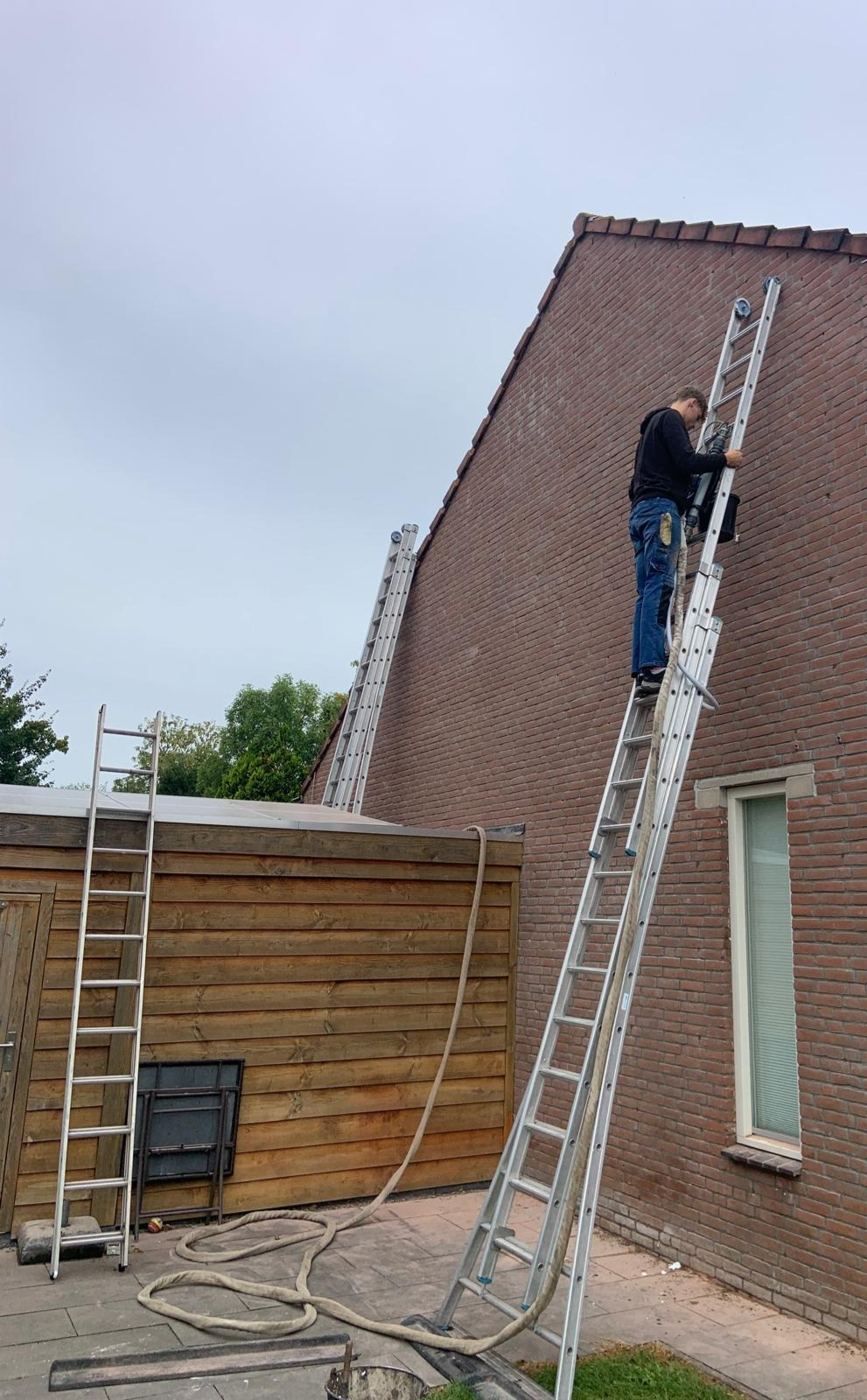 Monteur op een ladder bij de gevel van een woning